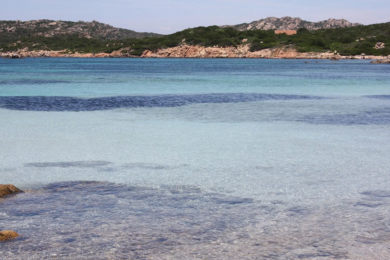 Acqua turchese e trasparente davanti alla costa granitica e alla macchia mediterranea dell'isola di Caprera